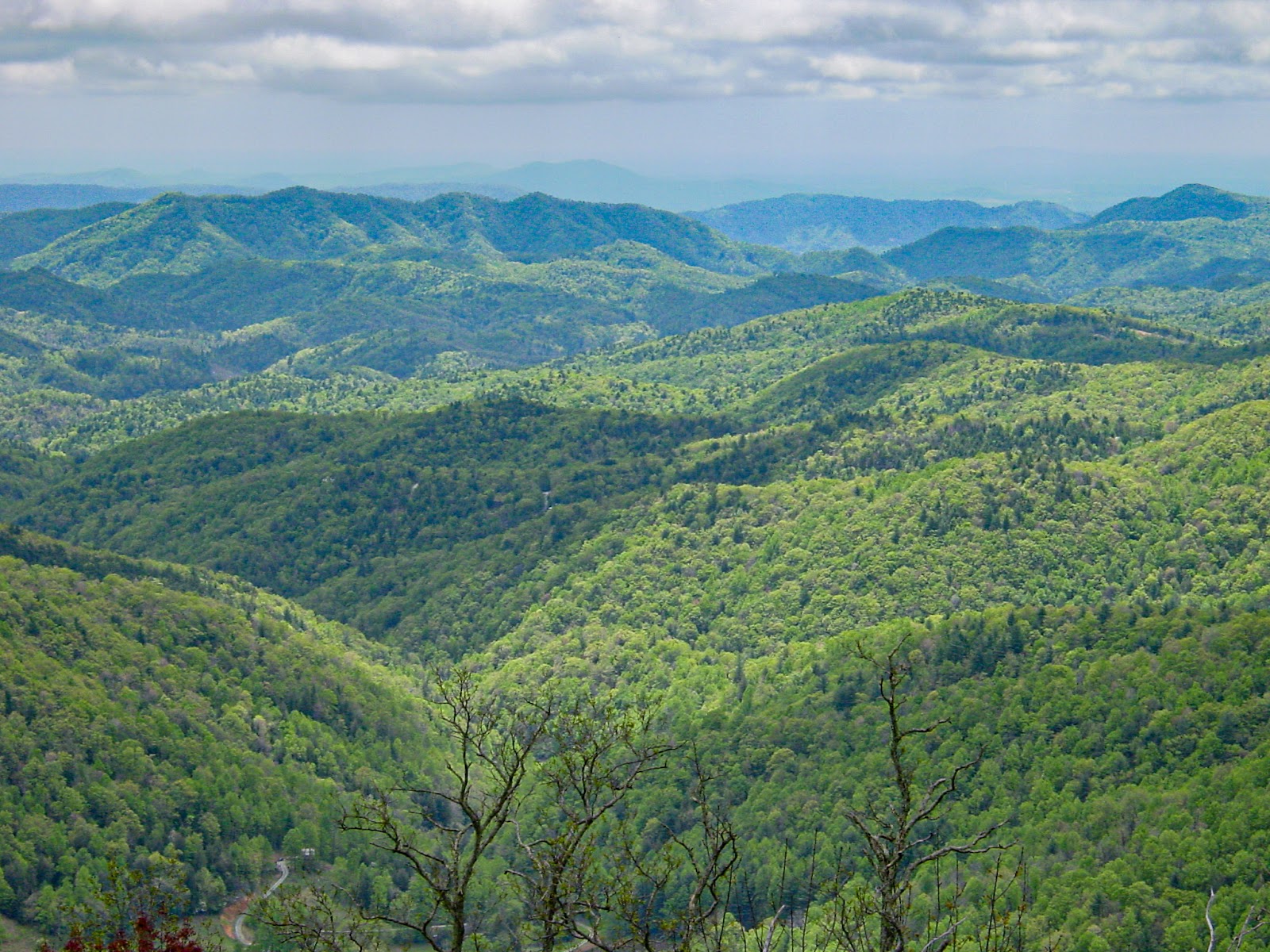 Clouds leave shadows on the contour of hills that fade into large mountains on the horizon. 