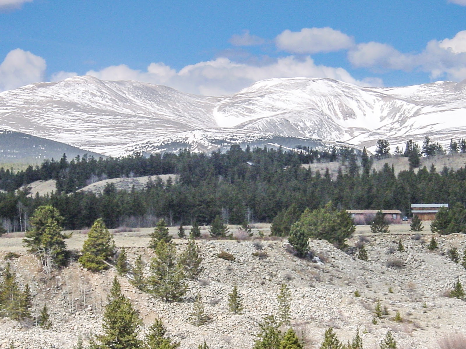 Big snowy mountains with a wooden ranch in the mid ground.