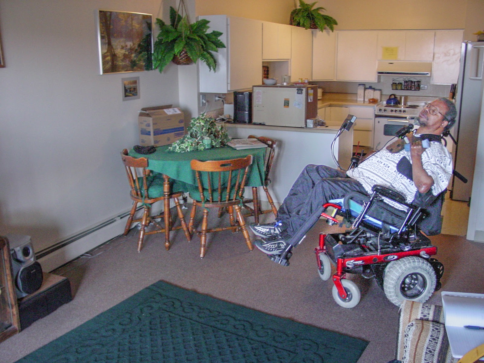 Man leaning back in his power wheelchair in an apartment