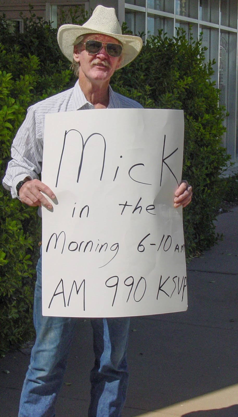 Man in cowboy hat and sunglasses holds a sign that says: MICK IN THE MORNING 6 - 10 AM AM 990 KSUP