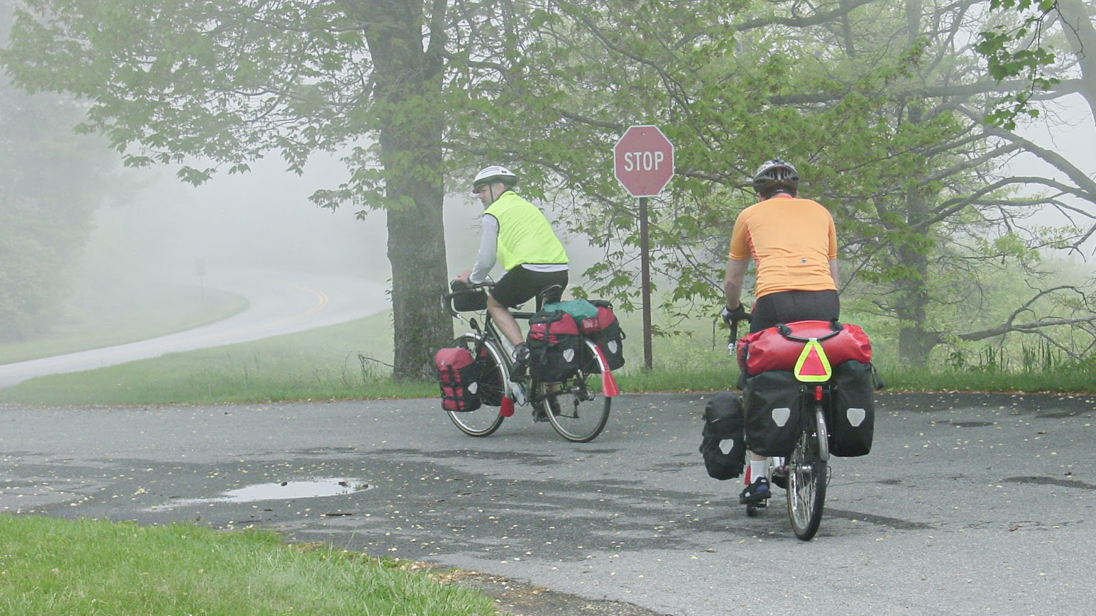Two cyclists with bikes loaded with camping gear ride into a fog. 
