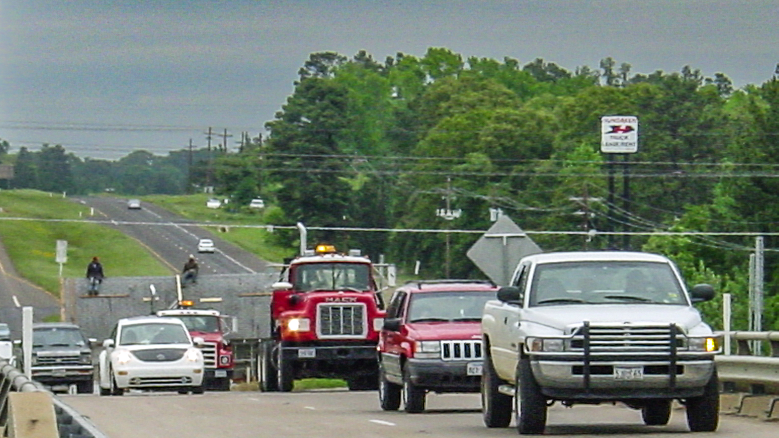 Cars on a bridge with two men sitting on the payload of a truck. 