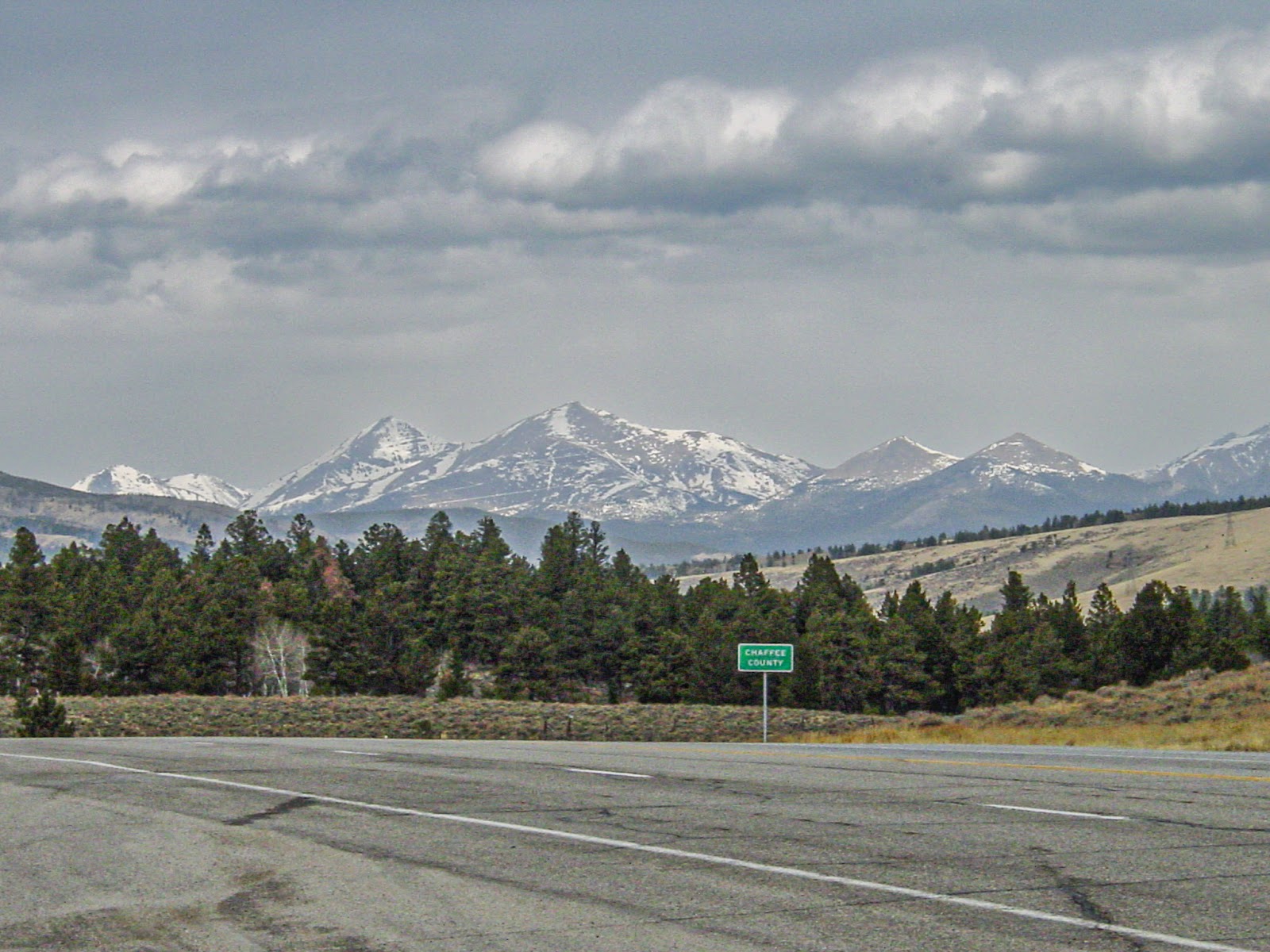 Dark skies and far-off snowy mountains in the background of a highway. A lone sign says: CHAFFEE COUNTY