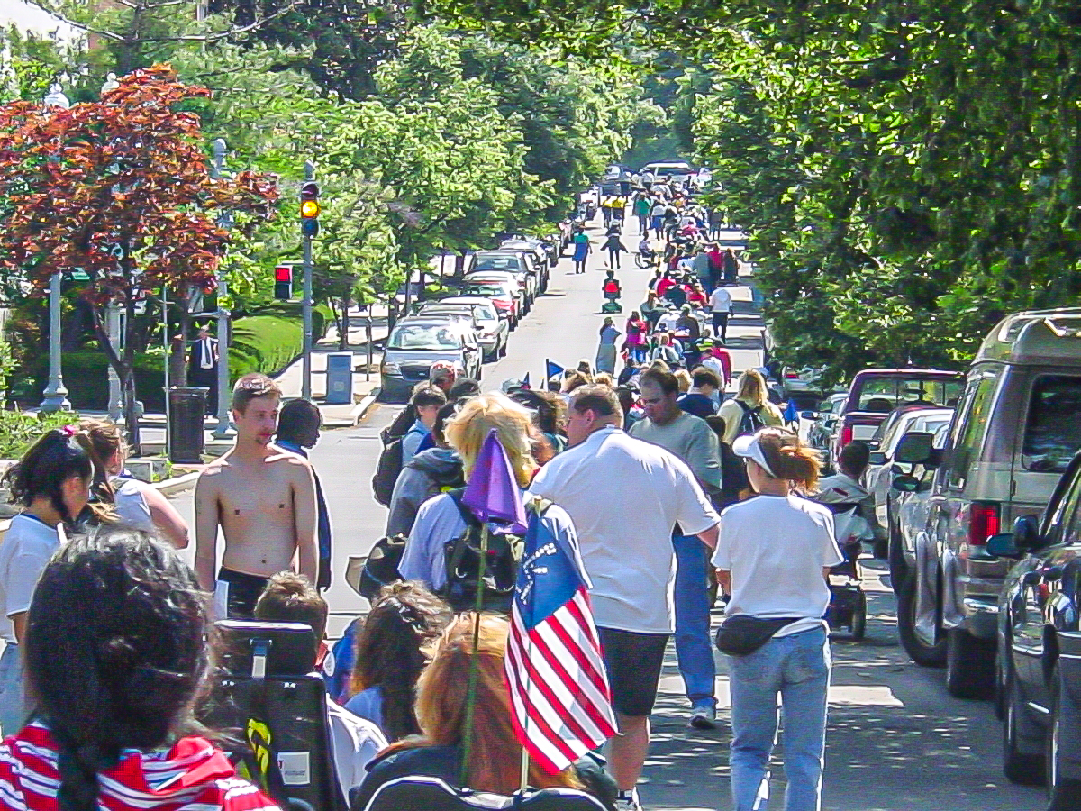 Colorful long line of people on one side of a road climbing up a hill. 