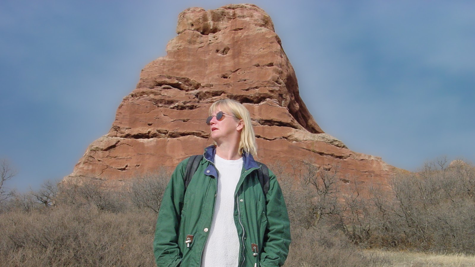 Woman in sunglasses with pointy reddish hill behind.