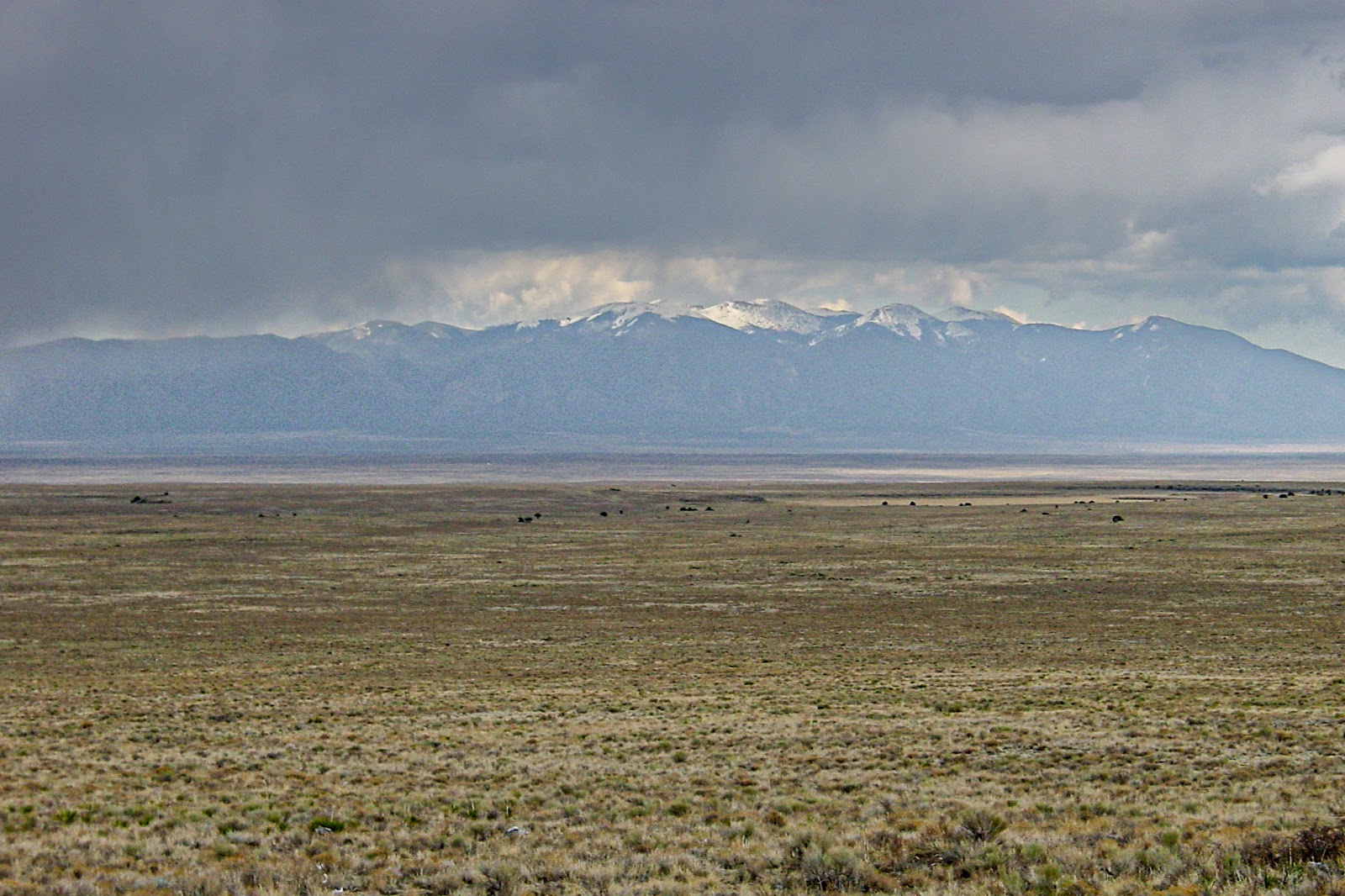 Stark, flat and barren landscape with dark snowy mountains in the distance and dark skies. 