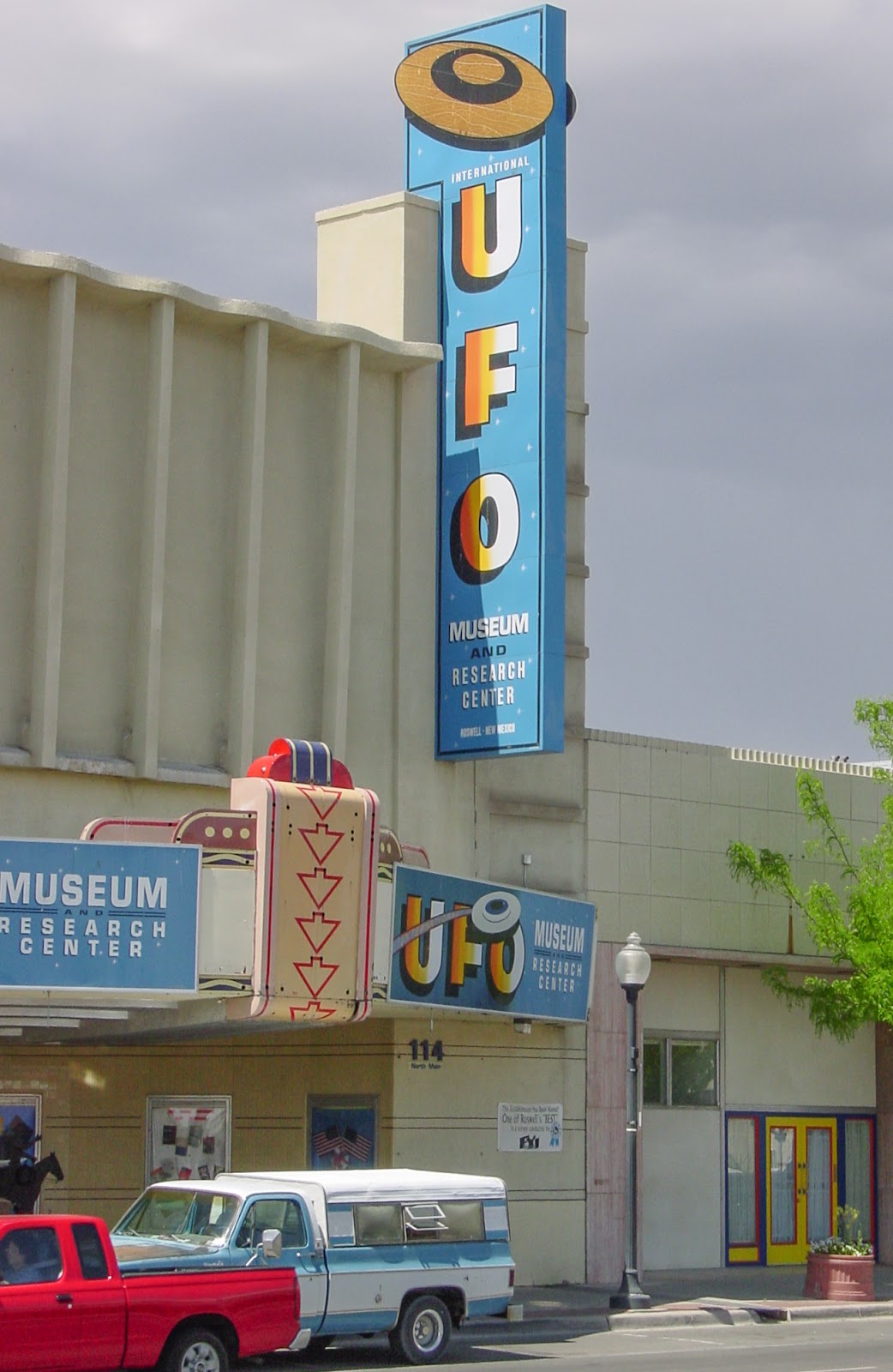 A small city street with an vertical sign that Reads: U F O Museum. 