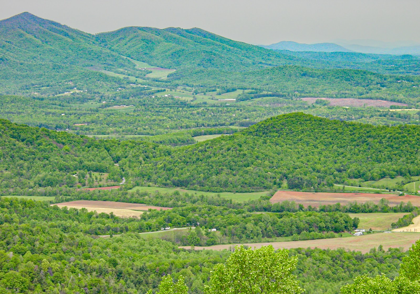 Tall mountains on the far side of a valley with many cleared farms between forested hills. 