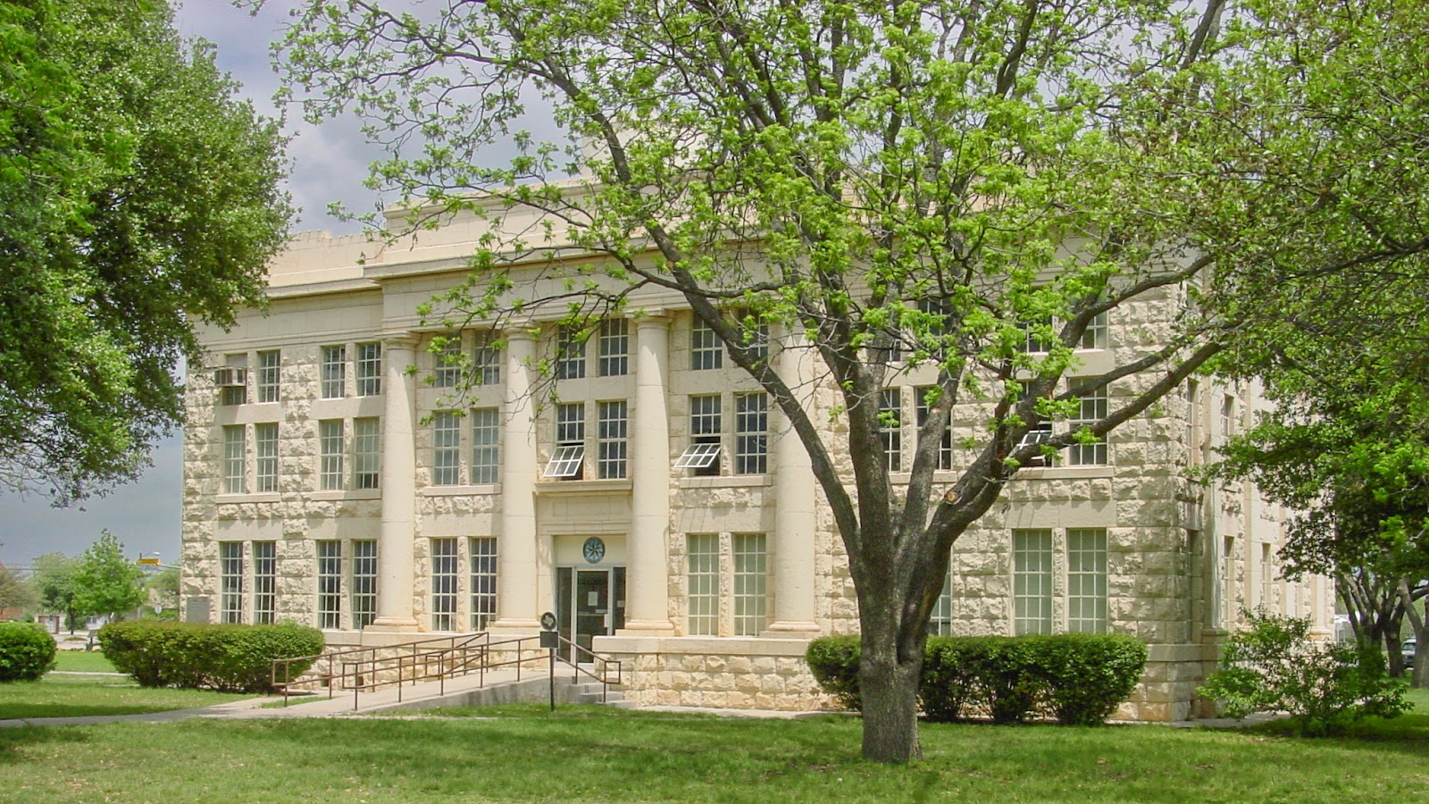A fieldstone three story building surrounded by trees.