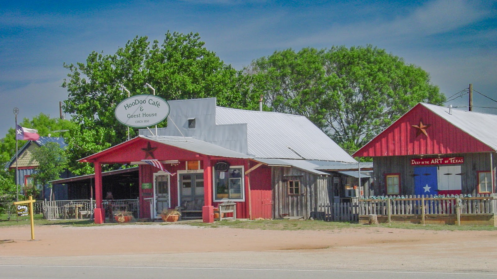 A brightly painted building with shiny new metal roof with a sign that reads: HooDoo Café and Guest House.