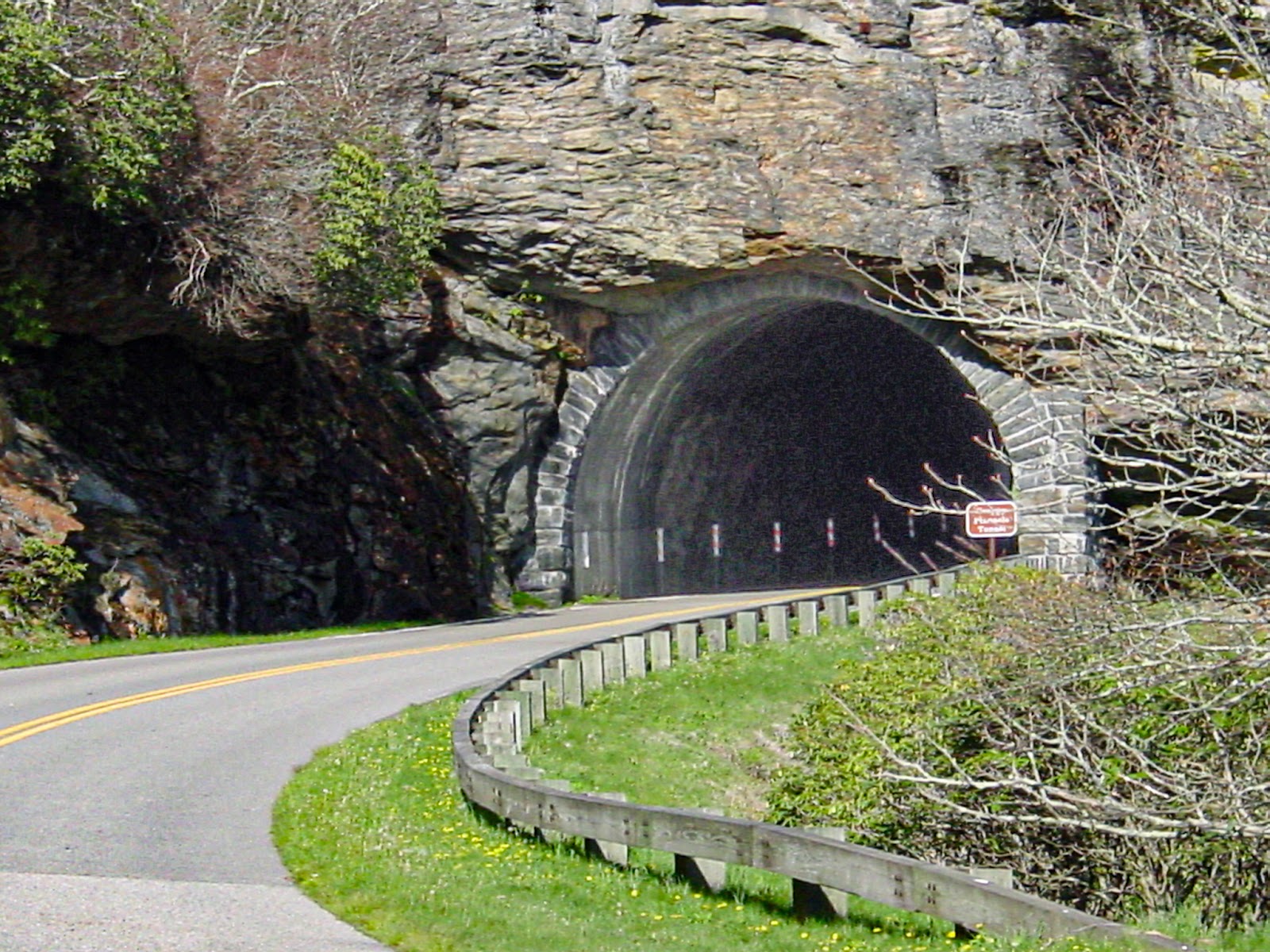A road curves into a dark tunnel cut into the mountain rock.