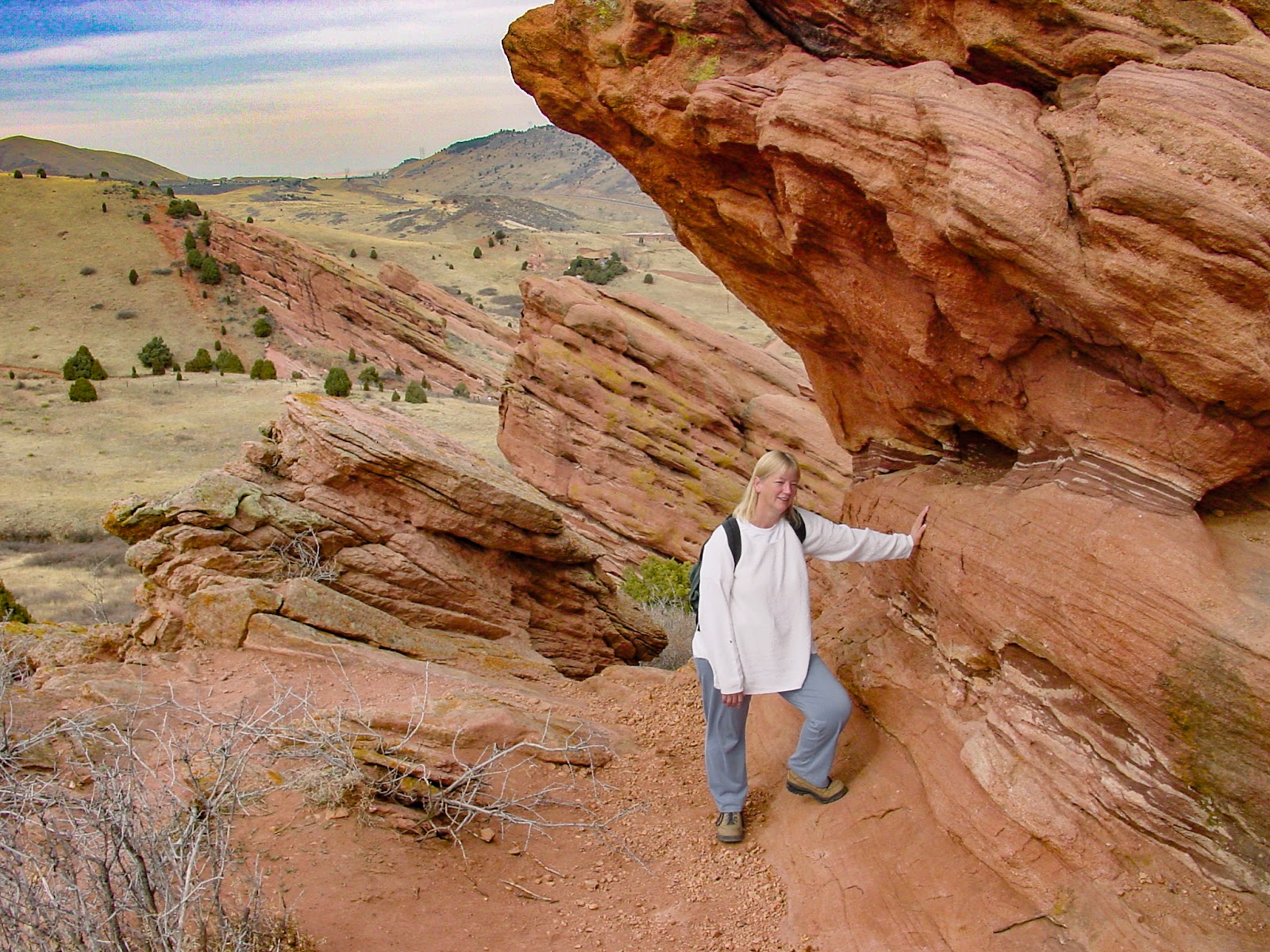 Woman leans on huge red rock with rocky landscape behind.