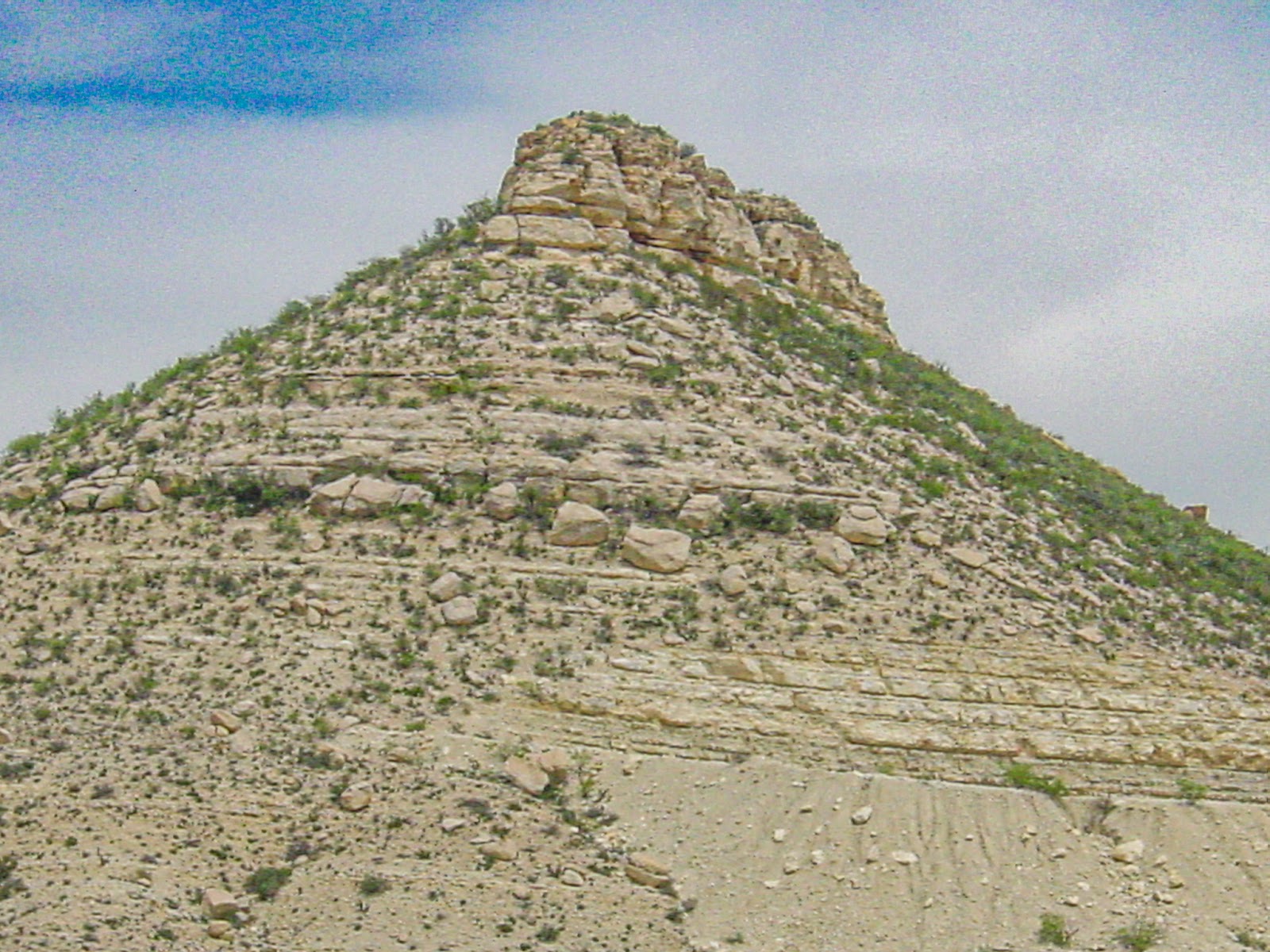 The top of a sandy hill with a grainy blue sky behind. 