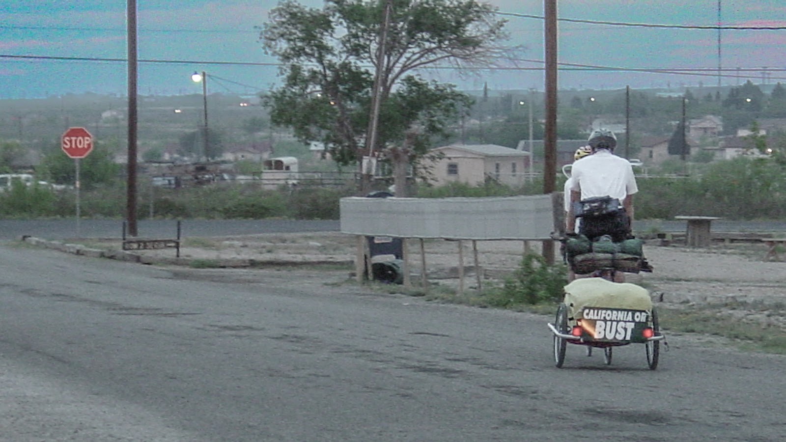 Two cyclists riding a tandem bike with a two wheel trailer. The sign on the back reads: CALIFORNIA OR BUST.