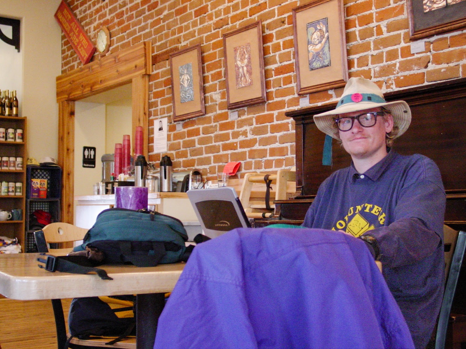 Man in wide-brimmed hat smiling working on a computer.