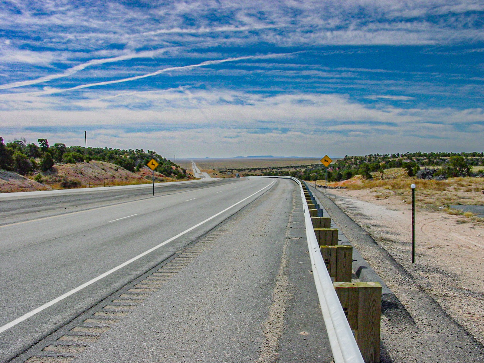 A highway disappears into the distant desert with cloudy blue skies above.