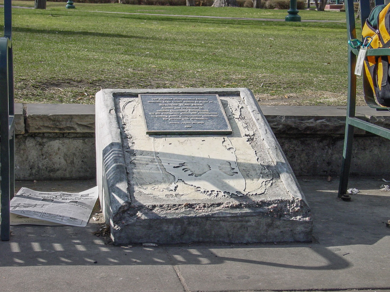 Rough and broken concrete pedestal for a plaque with trash surrounding it.