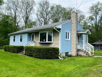 View of 136 Searles Road, Groton, NY 13073 from front. Shows front entrance, side entrance, picture window, stone finish on front and chimney.
