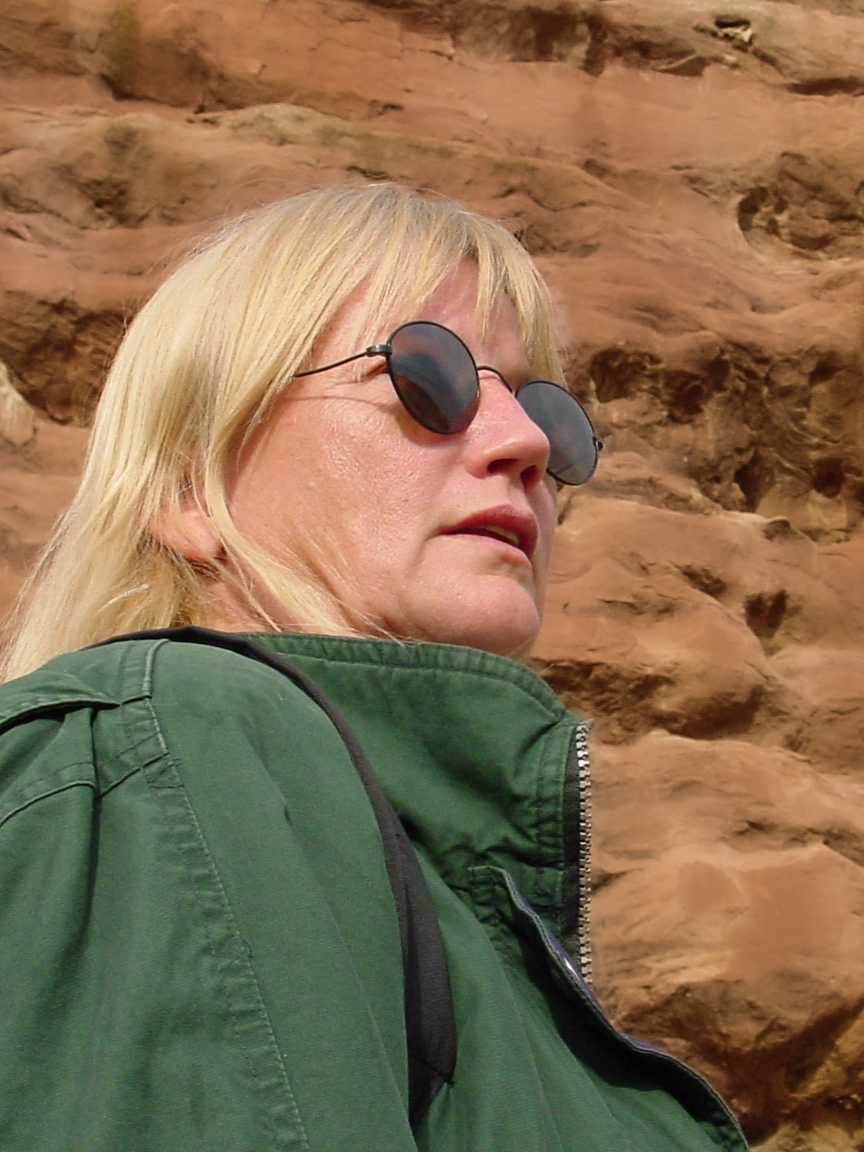Woman in sunglasses with reddish rocks behind. 
