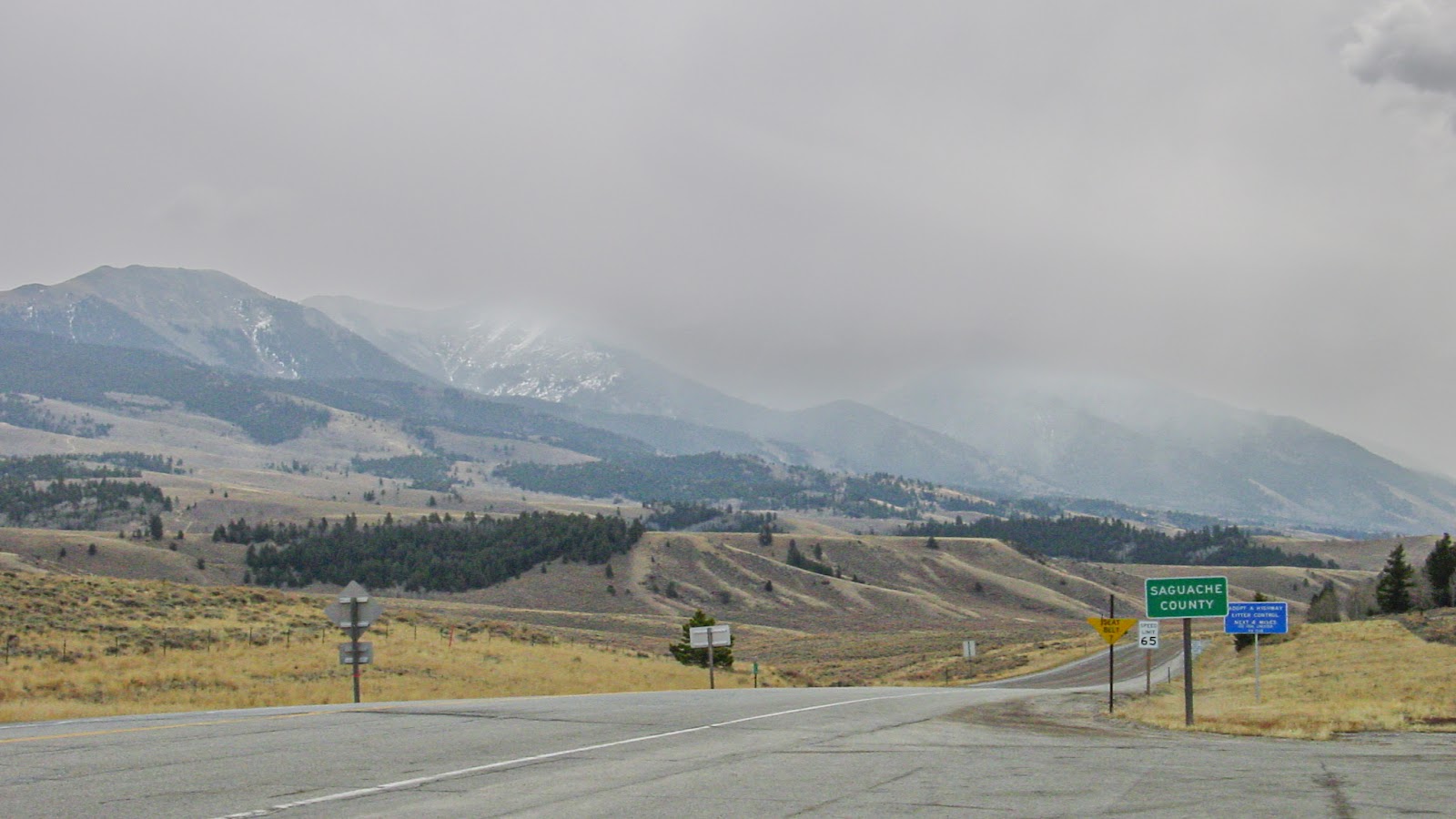 Distant misty mountains are behind a road and sign that says Saguachee County. 