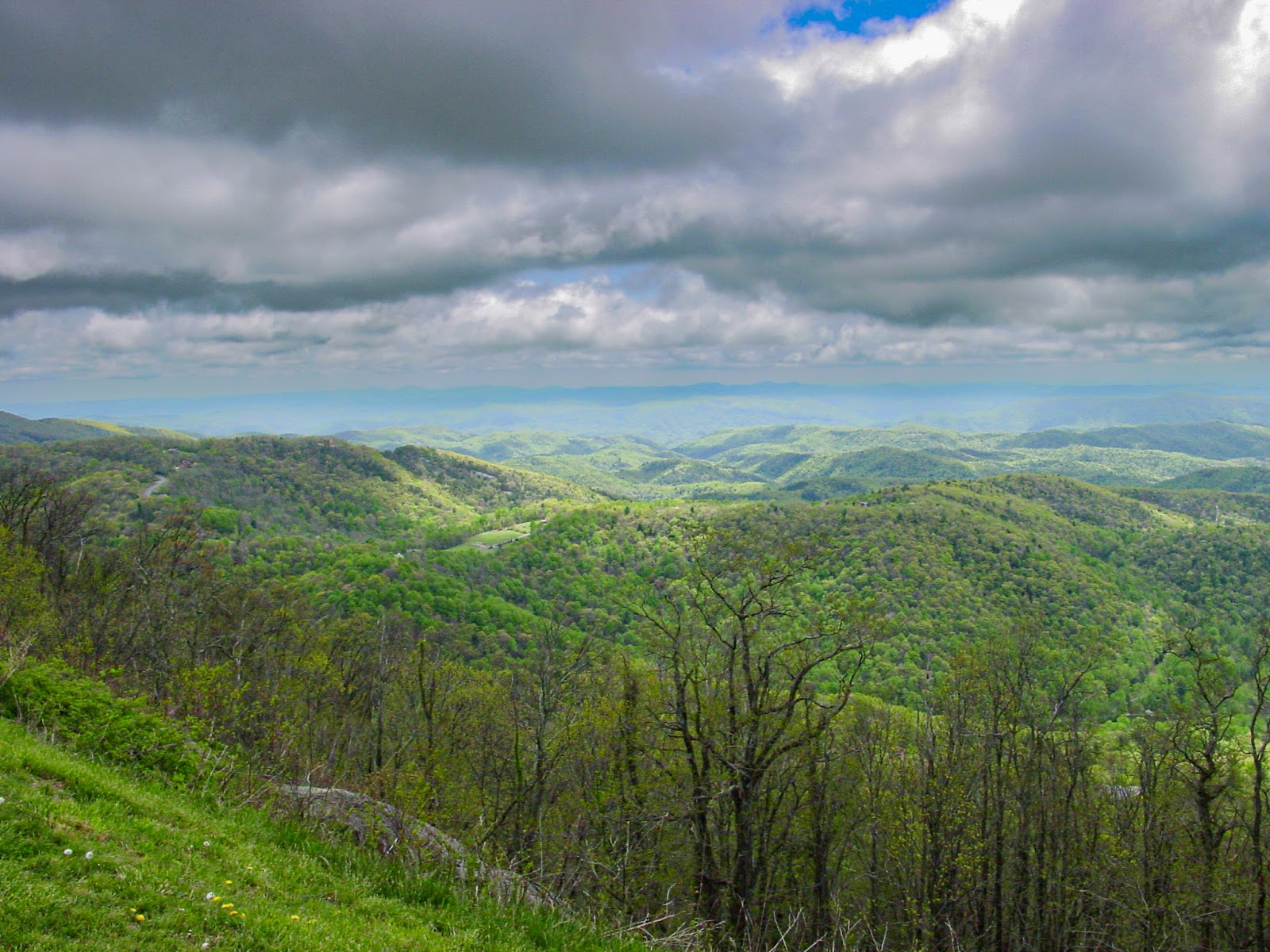 Low clouds make dramatic shadows on the hilly landscape with trees in the foreground. 