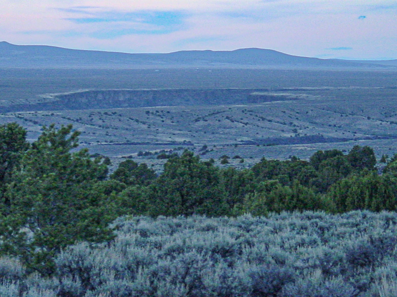 A gap opens in the landscape with desert shrubs in the foreground and mountains in the background. 