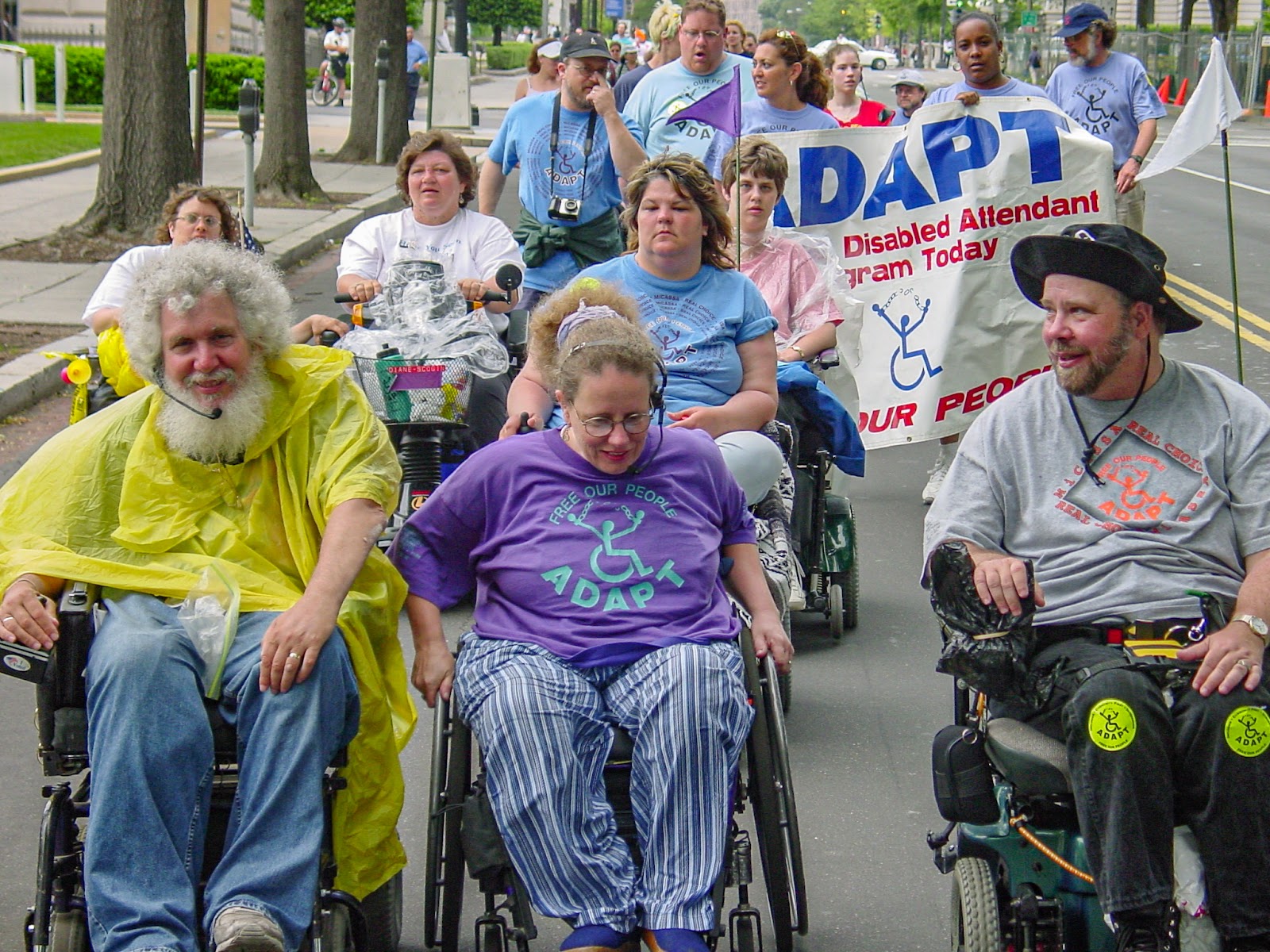 Three people in wheelchairs lead others in the street. 