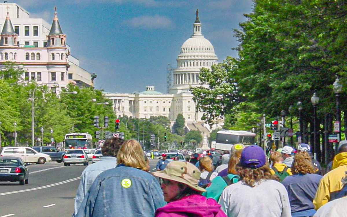 The US Capitol is ahead of many people walking in the street. 