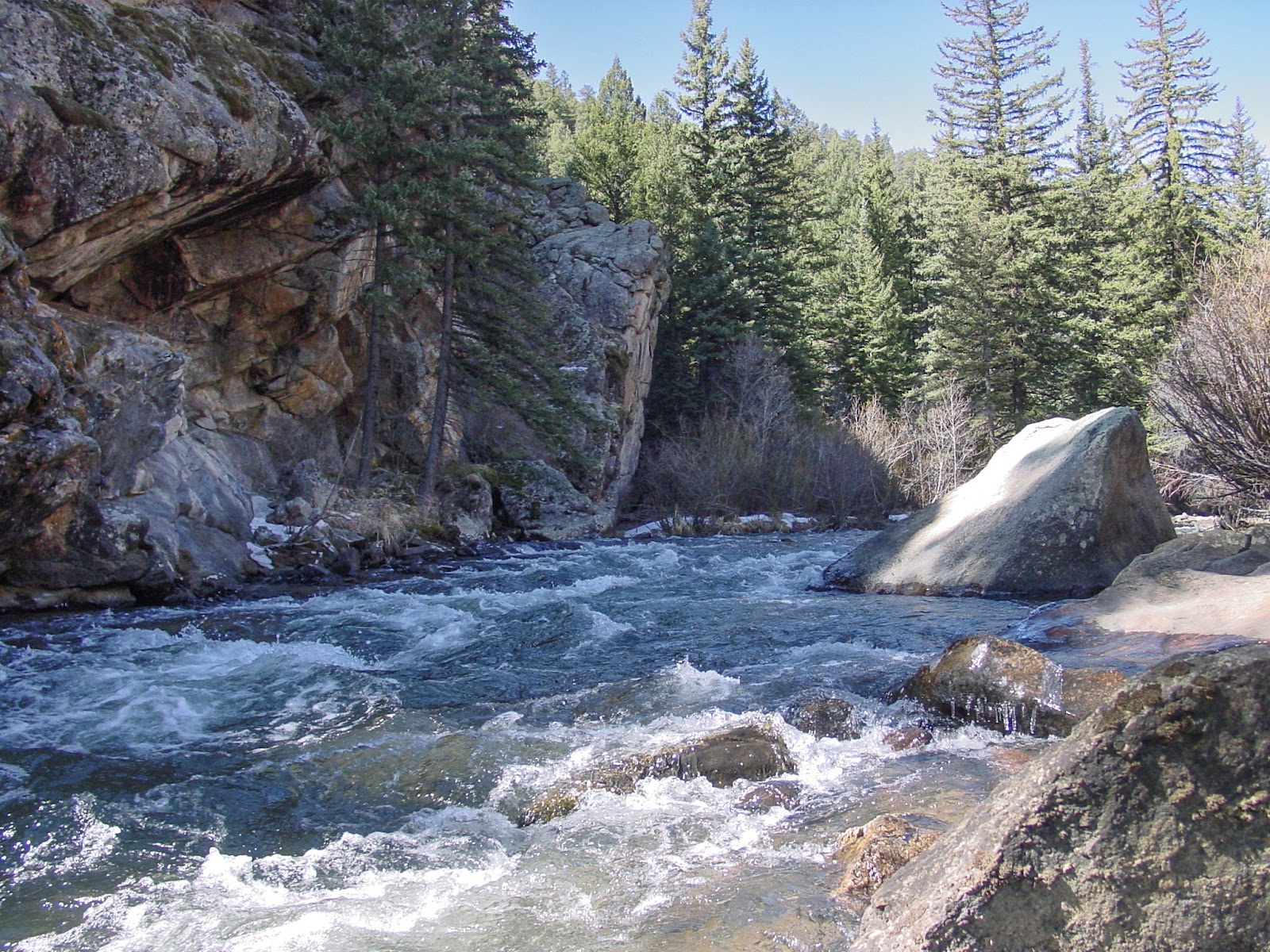 A fast creek runs past a shady cliff
