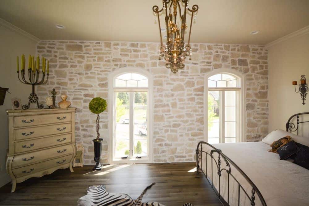 Primary bedroom with arched windows, a stone accent wall, and hardwood flooring topped by a zebra rug.