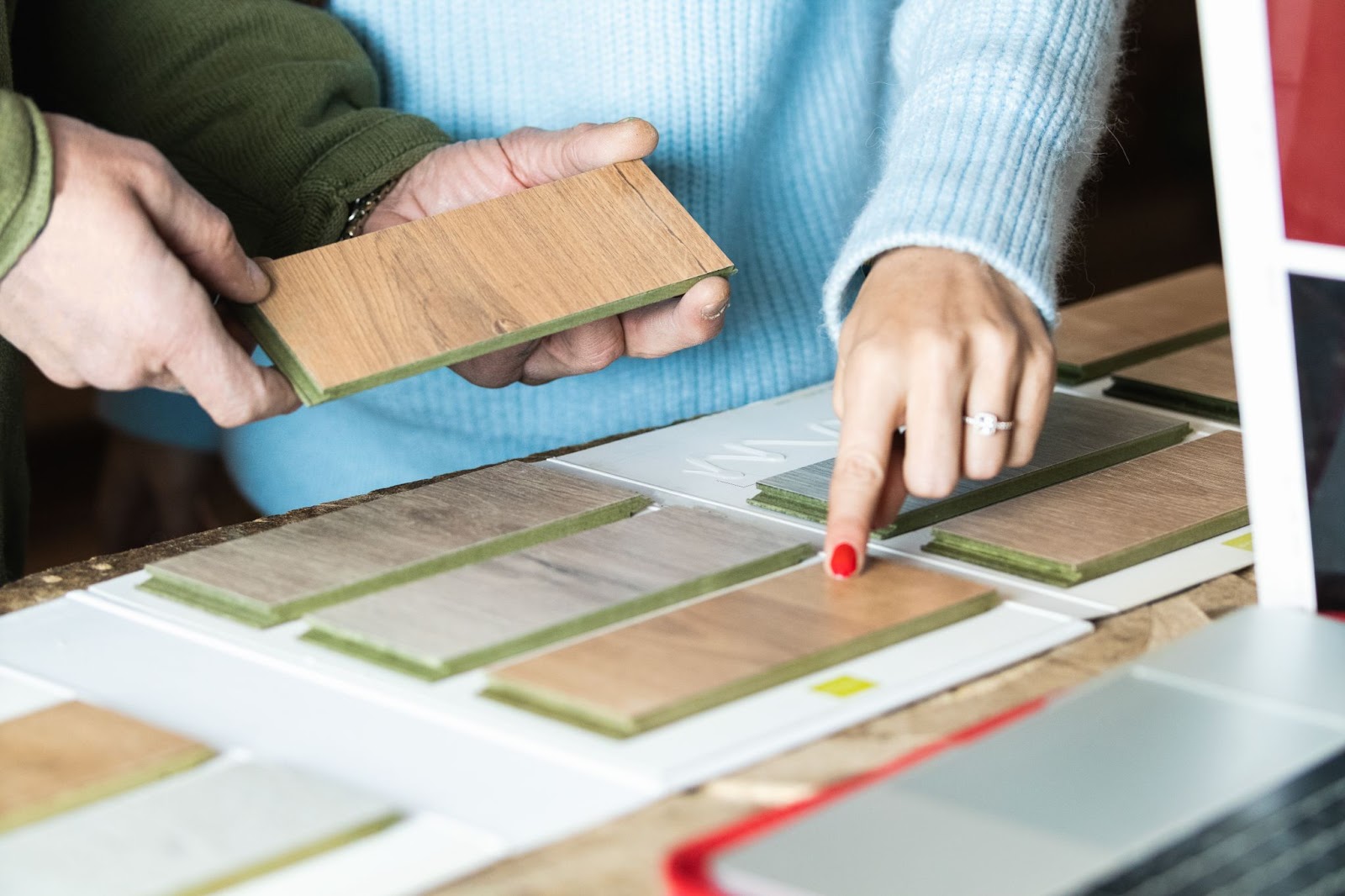 An anonymous woman selects a flooring design from the sample blocks while a carpenter assists her in a workshop.