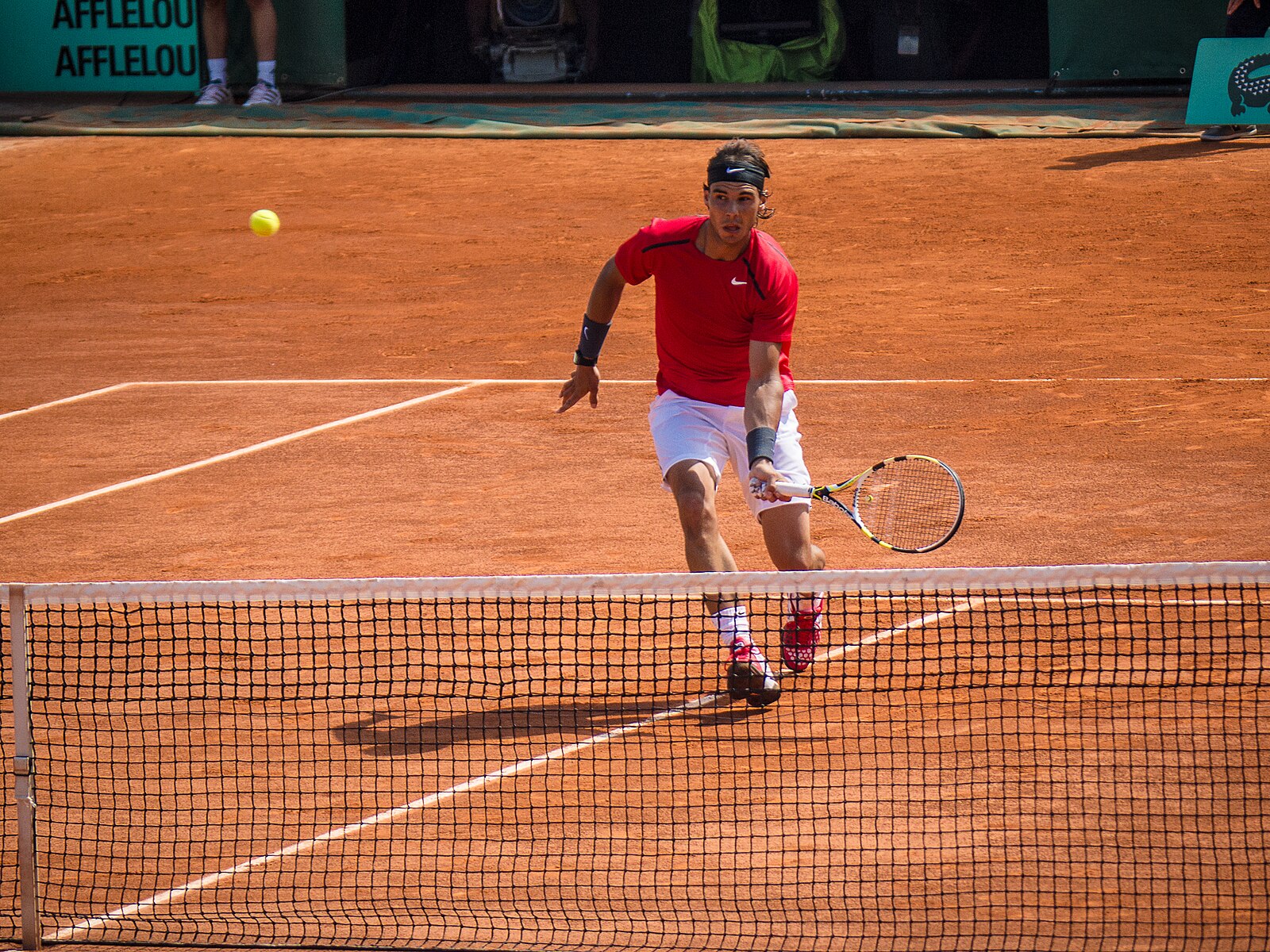 Rafael Nadal se aproximando da rede em uma partida de tênis no saibro