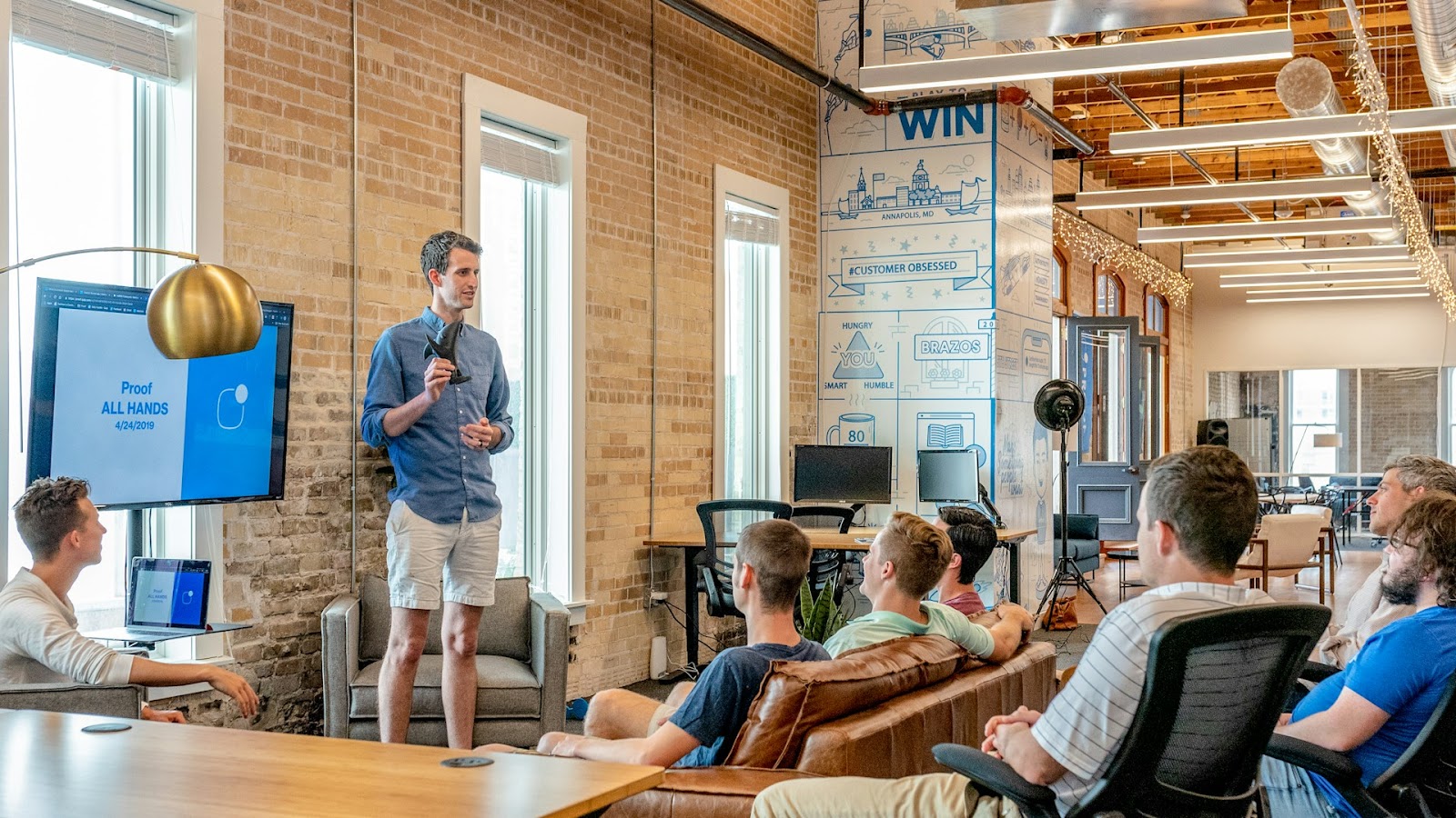 A presenter leading a weekly business review meeting in a modern, open office space.