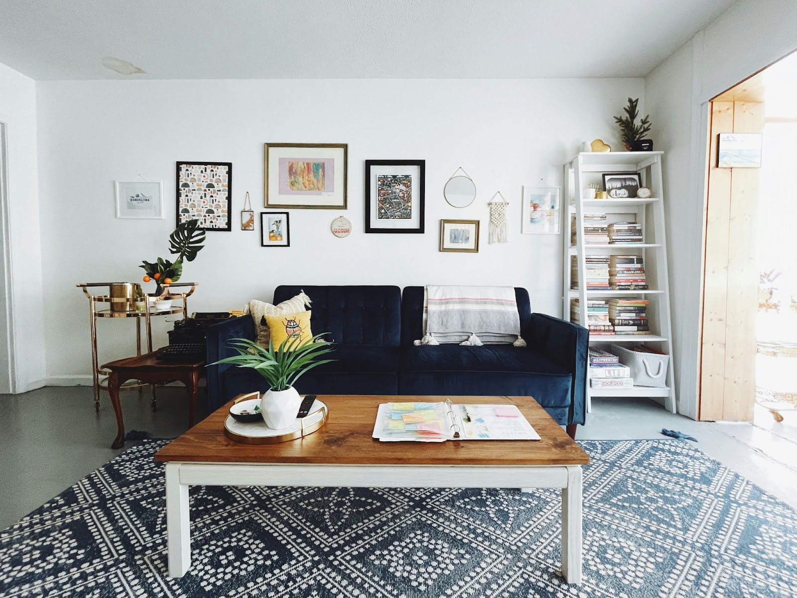 A stylish living room showcasing the Airbnb business model, featuring a navy blue sofa, a wooden coffee table, a patterned rug, a gallery wall, and a bookshelf.