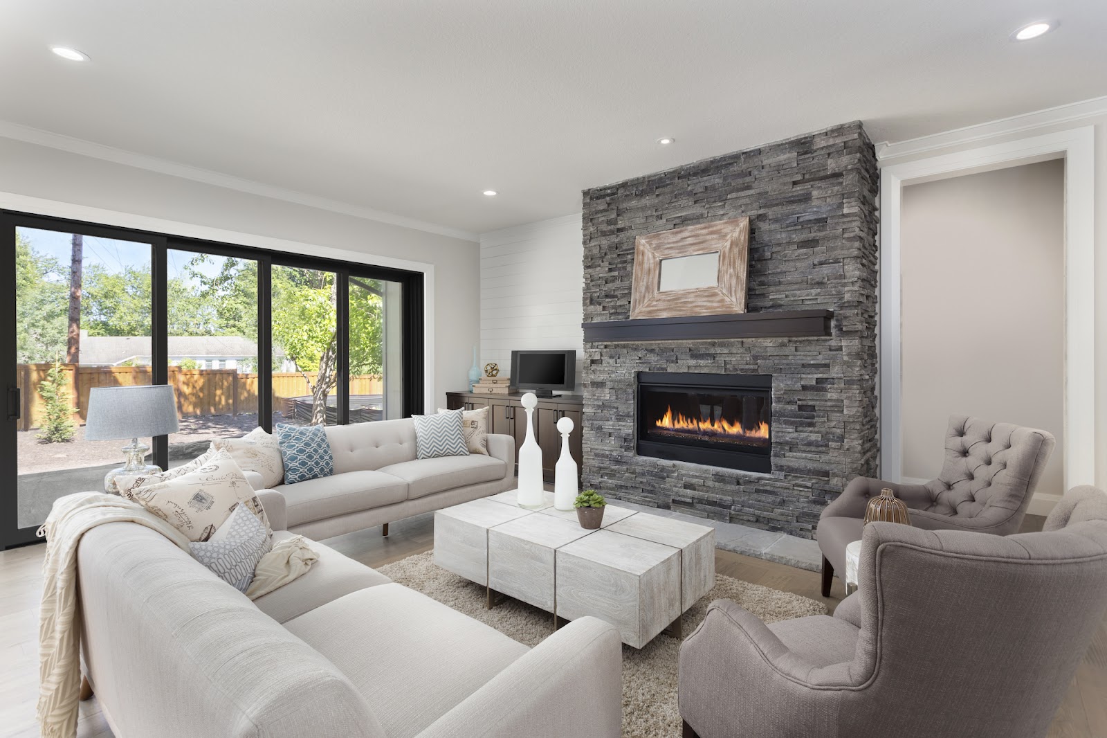 A living room with a lit fireplace has a sliding glass door with black trim that leads out onto a patio.