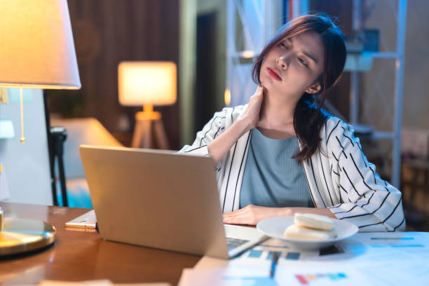 A person sitting at a desk with her hand on her neck  Description automatically generated