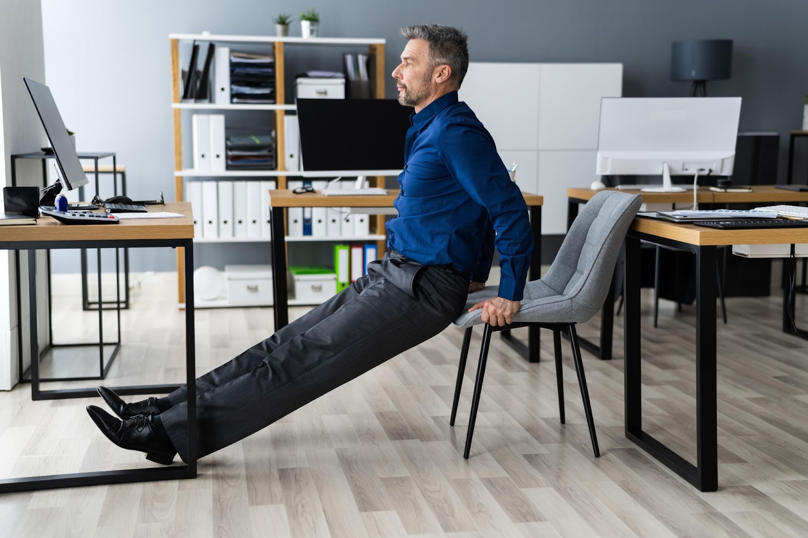 A man stretching his leg while working at a standing desk, a good practice for ergonomics.