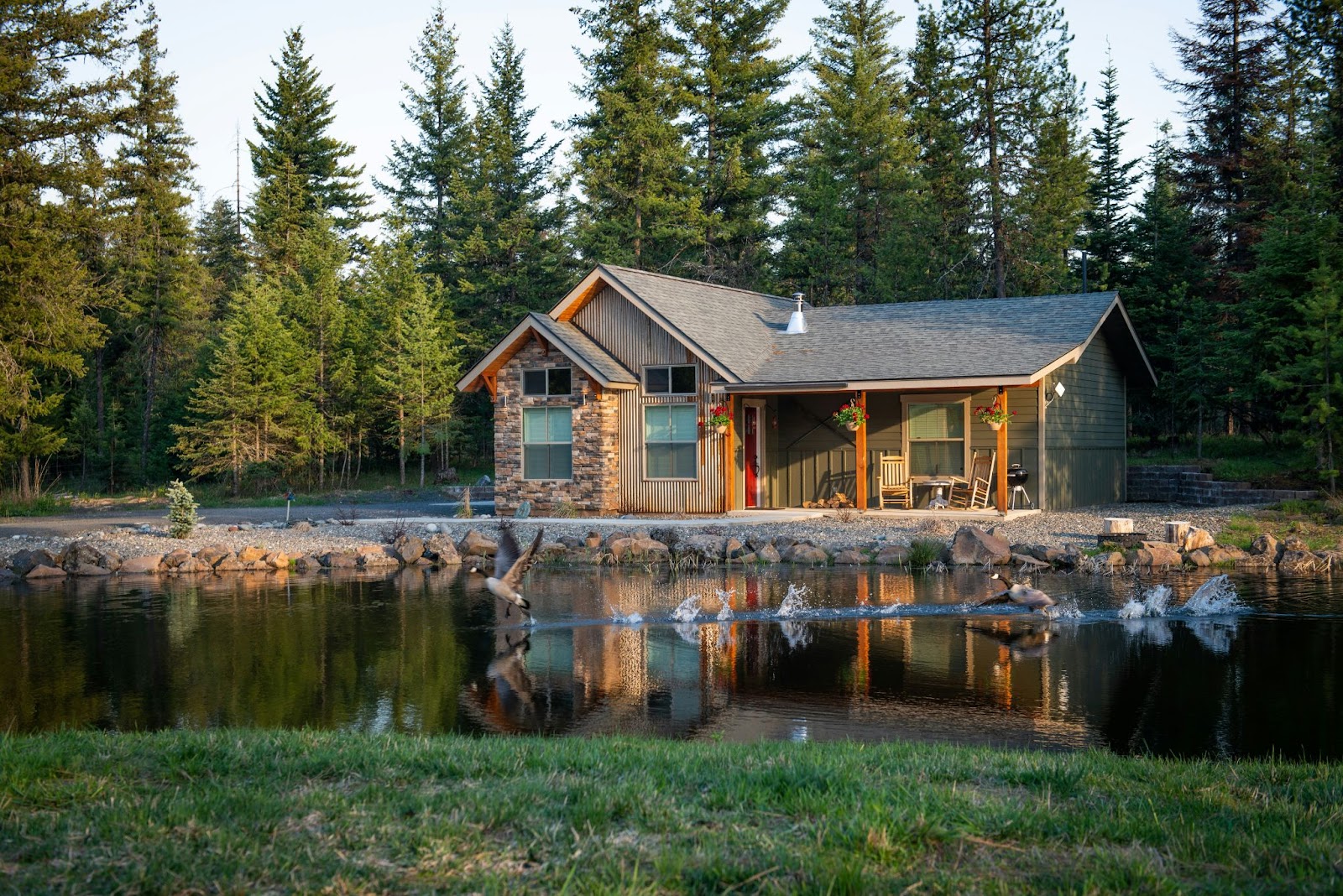 A cozy cabin-style house, perfect for the Airbnb business model sits beside a tranquil pond, featuring a stone and wood exterior, a covered porch, and rustic charm.