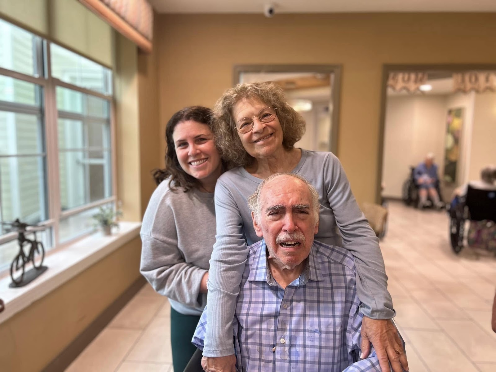 A senior citizen smiling in an assisted living facility with family