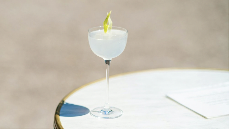 A daiquiri is on a white marble table in the sunshine with a decorative lime garnish