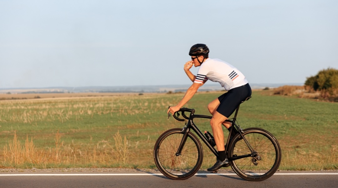 Muscular athletic man eating while cycling on the road.