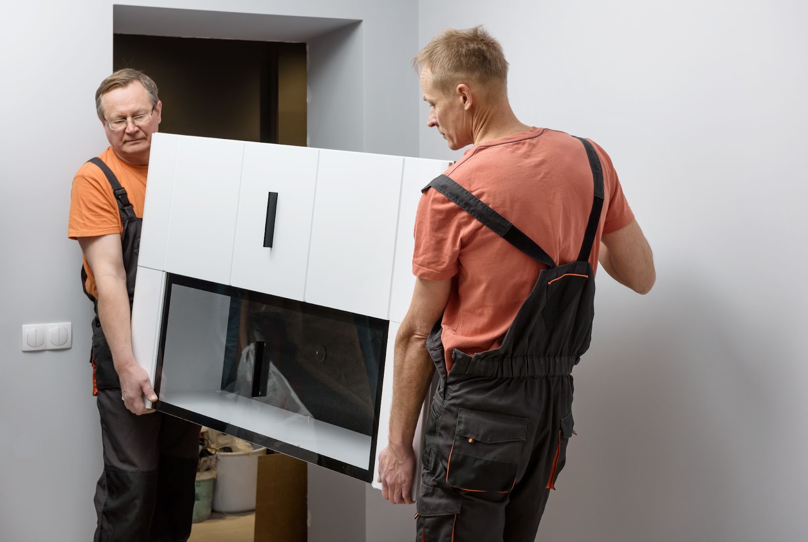 A pair of movers carry a large dresser into a home. 