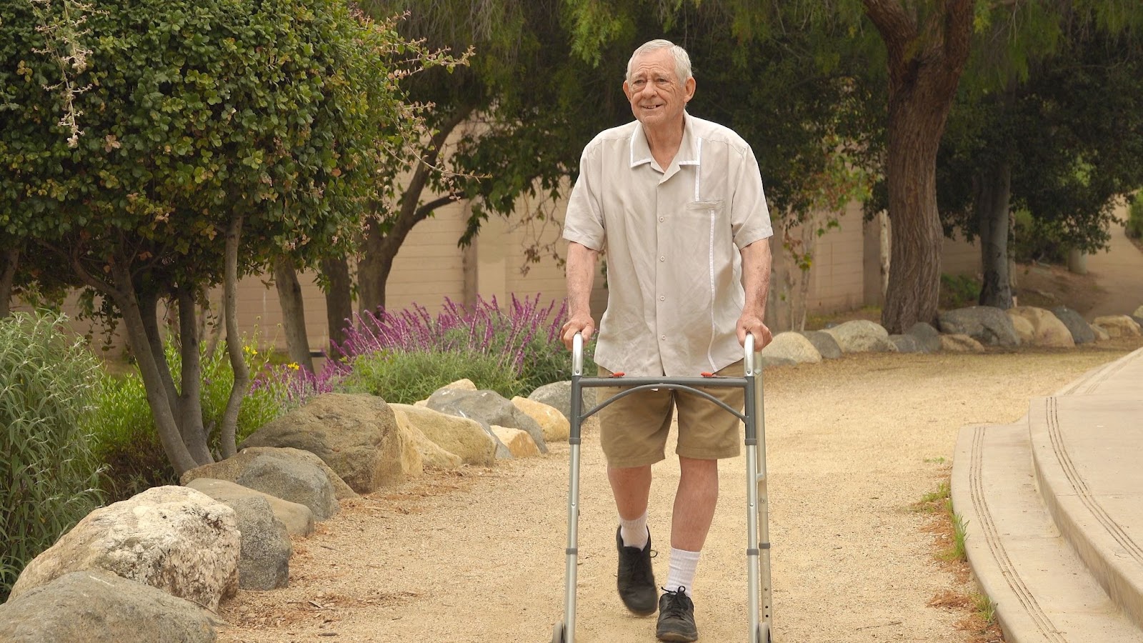 A happy senior with a walker goes for a walk on a well-maintained trail.