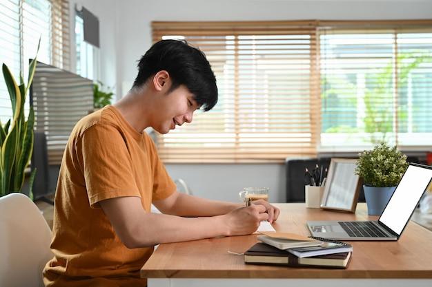 Premium Photo | Side view smiling man sitting in front of laptop computer  and making notes on notebook