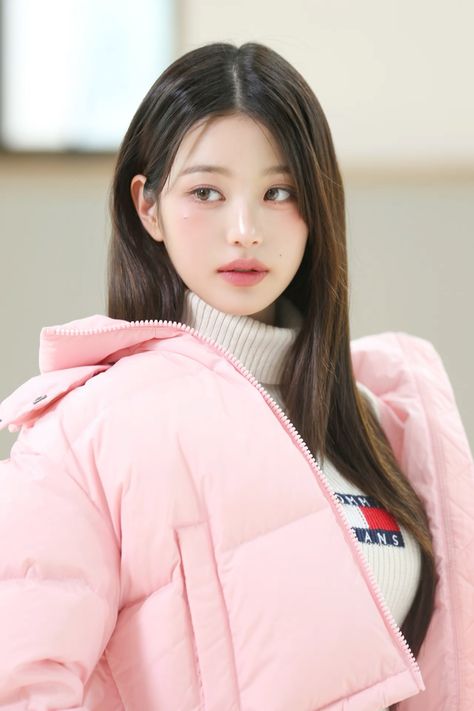  This contains an image of IVE's Jang Wonyoung with her long hair wearing a pink puffy jacket and turtle neck sweater, looking at the camera