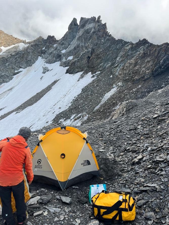 A person standing next to a tent on a rocky mountainAI-generated content may be incorrect.