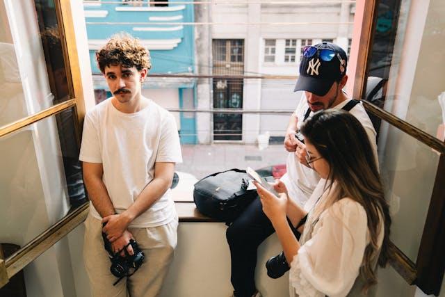 Three people dressed in light clothing standing beside a window