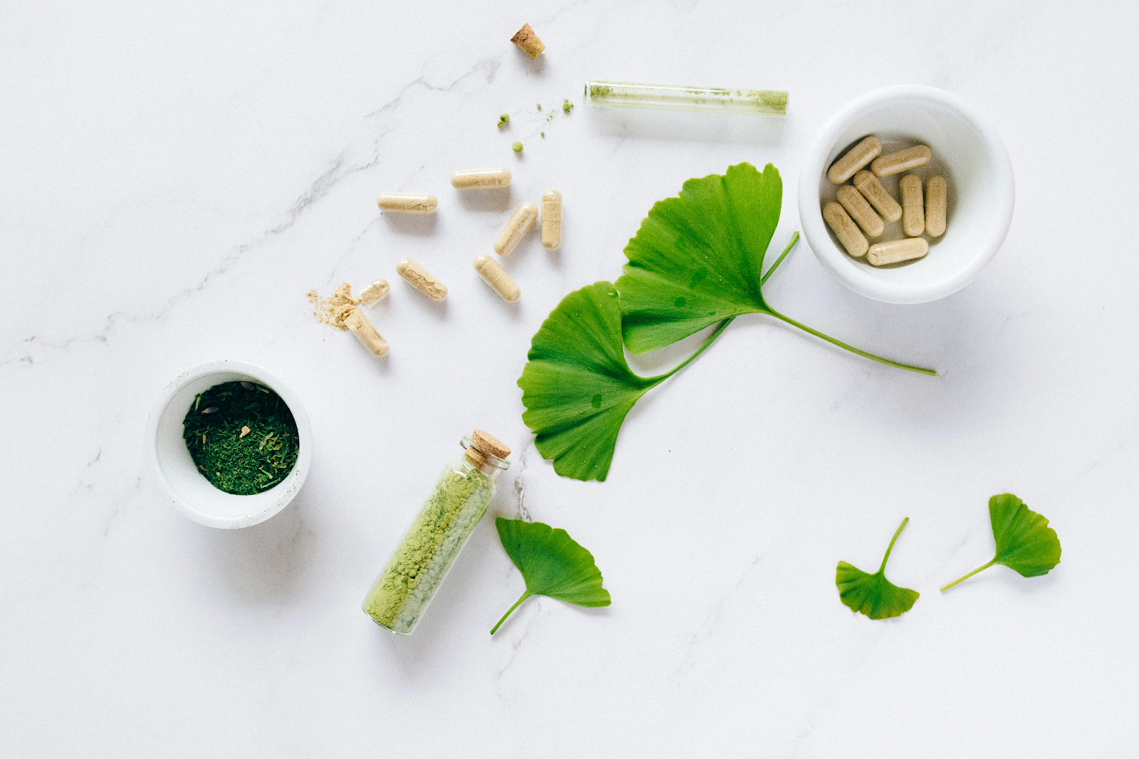 Few types of medicine. In powder, in pill with leaves around it on  white surface.