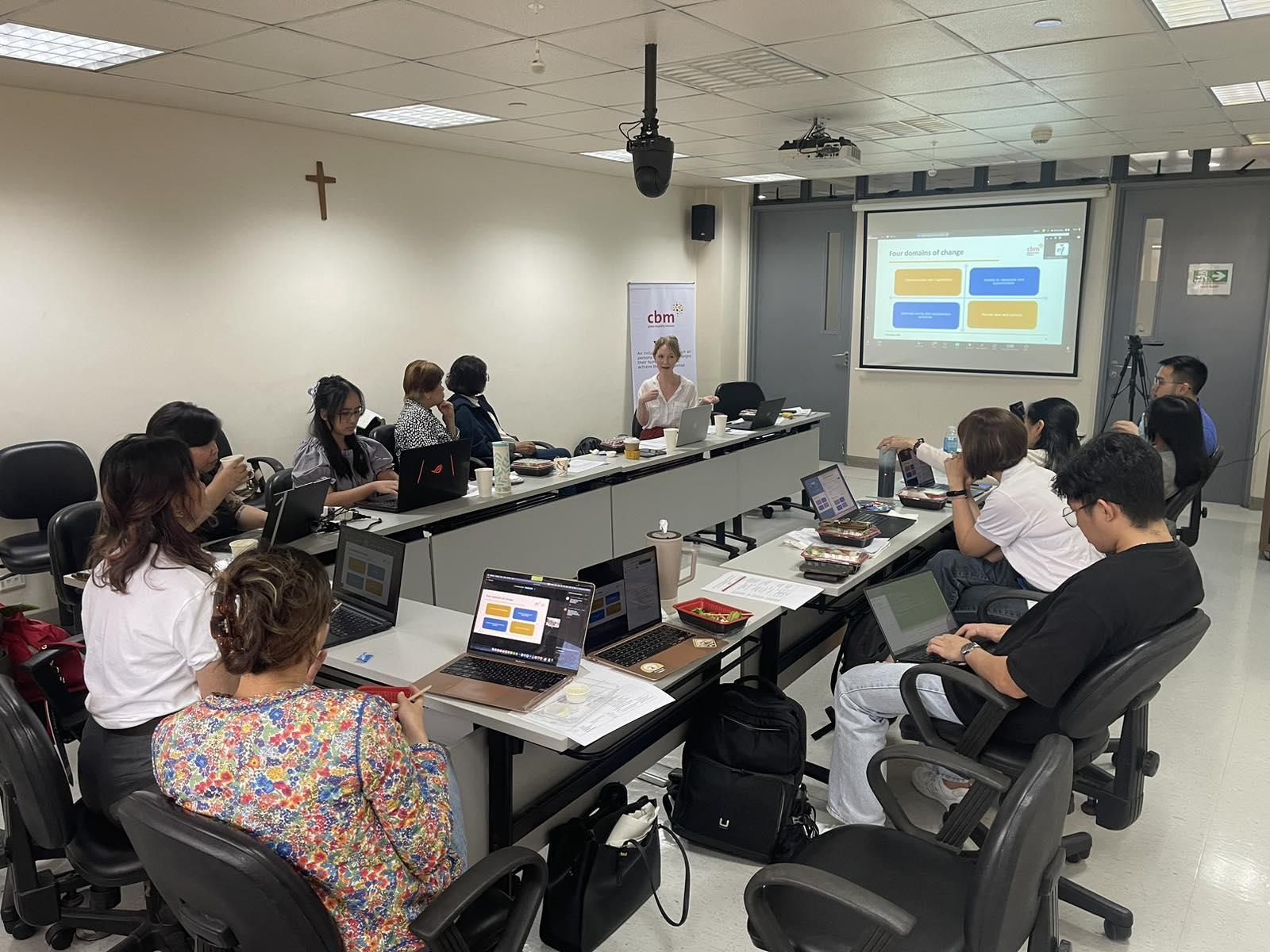 A photo of Teresa Lawler, Senior Disability Inclusion Advisor from CBM Australia, and her presentation, facing the rest of the Rise and Thrive program team during a discussion.