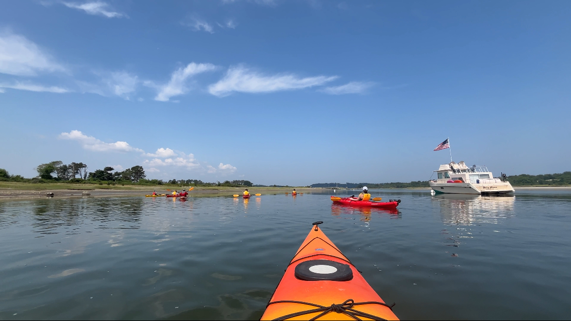 POV sitting in an orange kayak on calm waters in Castle Neck River on the Crane Estate in Ipswich, Massachusetts